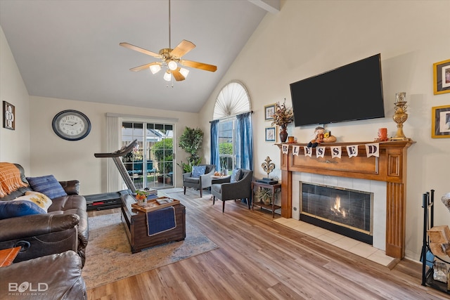 living room featuring ceiling fan, light hardwood / wood-style floors, high vaulted ceiling, and a tile fireplace