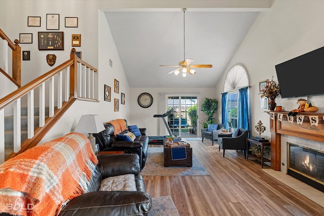 living room with ceiling fan, beamed ceiling, light hardwood / wood-style flooring, high vaulted ceiling, and a tile fireplace