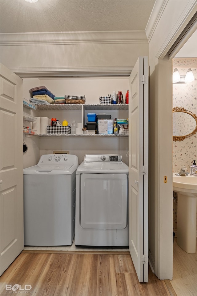 laundry room featuring light wood-type flooring, crown molding, sink, and washing machine and dryer