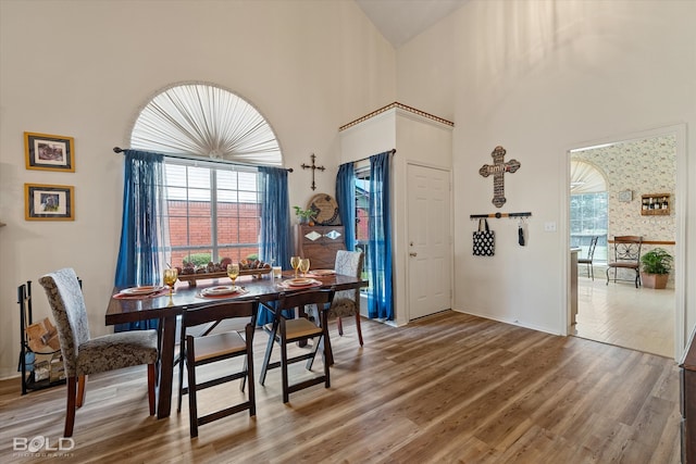 dining space with a towering ceiling, plenty of natural light, and wood-type flooring