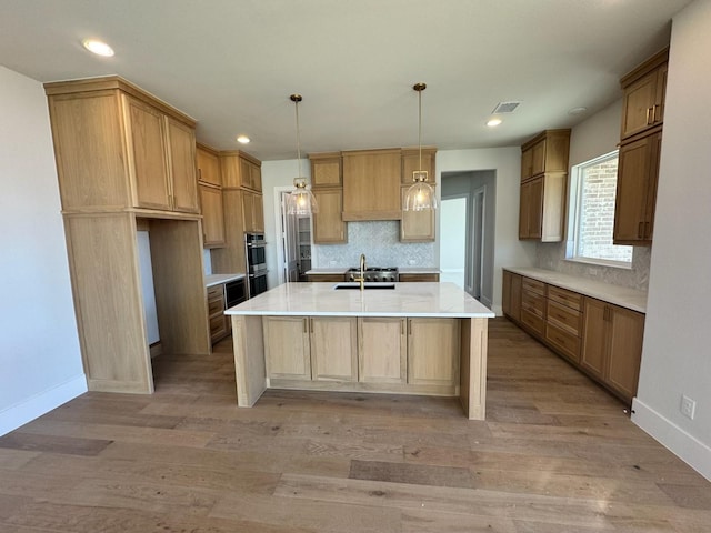 kitchen featuring pendant lighting, stainless steel double oven, an island with sink, sink, and light hardwood / wood-style flooring