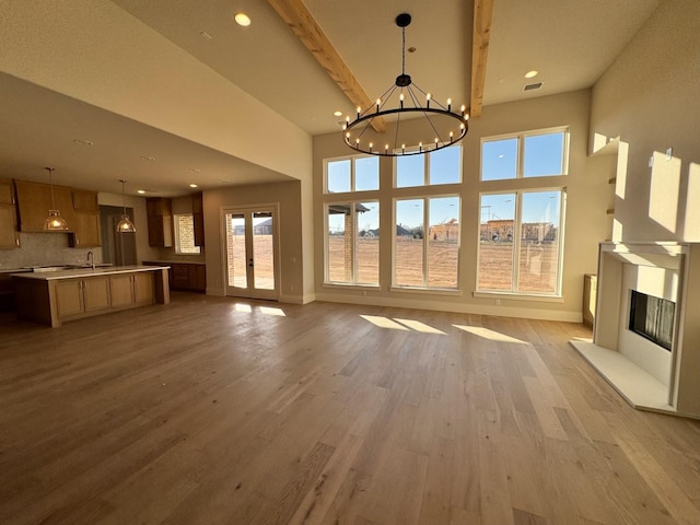 unfurnished living room featuring a healthy amount of sunlight, beamed ceiling, a chandelier, and light hardwood / wood-style floors