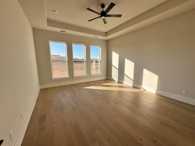 spare room featuring light wood-type flooring, ceiling fan, and a raised ceiling