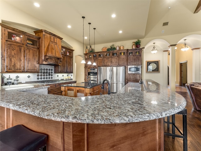 kitchen featuring a large island with sink, dark hardwood / wood-style floors, stainless steel appliances, vaulted ceiling, and decorative light fixtures