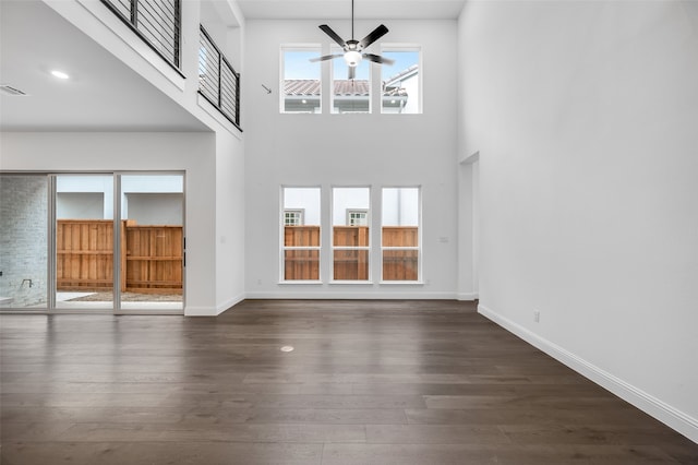 unfurnished living room with a high ceiling, dark wood-style flooring, a ceiling fan, and baseboards