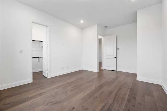 unfurnished bedroom featuring baseboards, dark wood-style flooring, a walk in closet, a closet, and recessed lighting