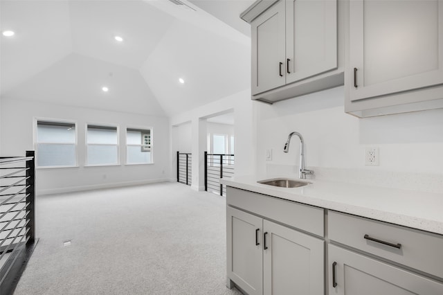 kitchen with lofted ceiling, light stone counters, light colored carpet, a sink, and gray cabinets