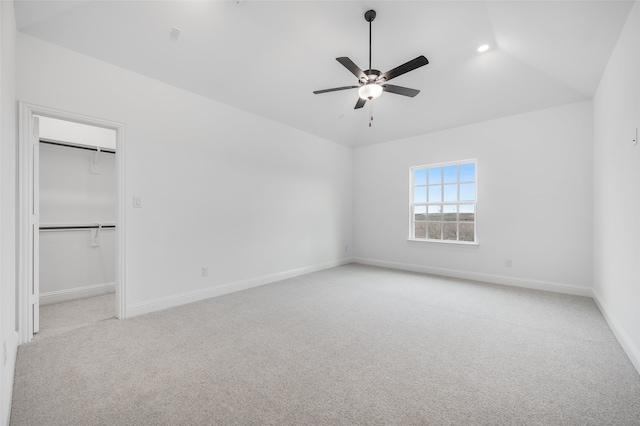 unfurnished bedroom with a spacious closet, baseboards, vaulted ceiling, and light colored carpet