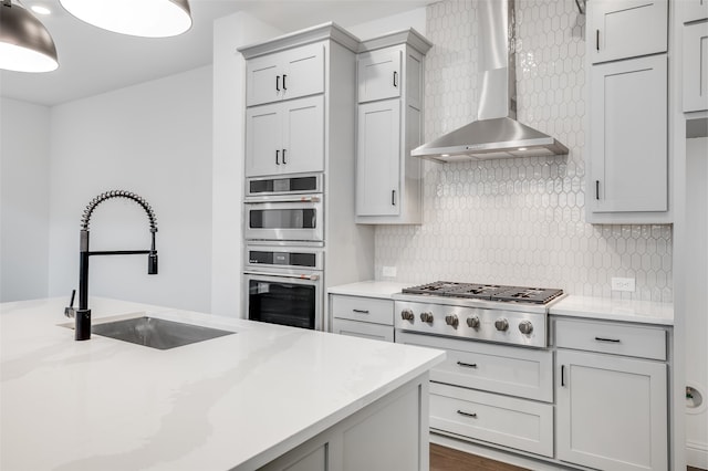 kitchen featuring wall chimney exhaust hood, stainless steel appliances, a sink, and gray cabinetry