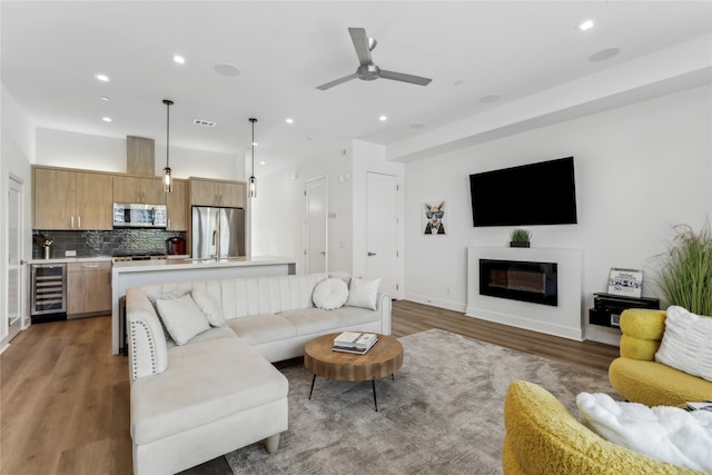 living room featuring ceiling fan, sink, wine cooler, and dark hardwood / wood-style flooring