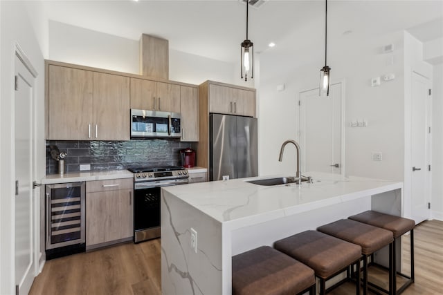 kitchen with wine cooler, sink, light stone counters, decorative light fixtures, and stainless steel appliances