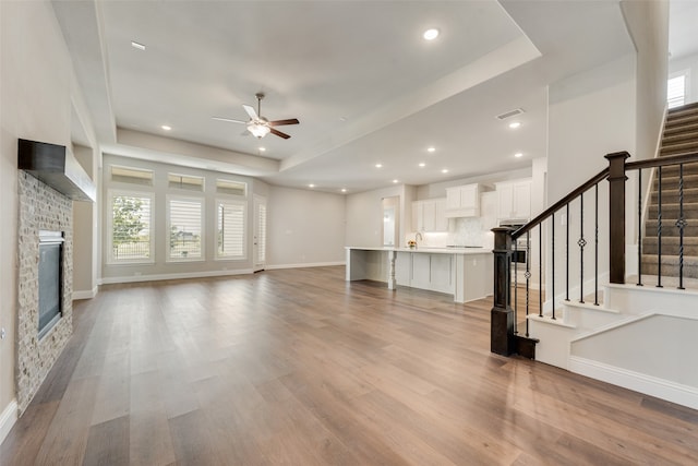 unfurnished living room with light wood-type flooring, a tray ceiling, and ceiling fan