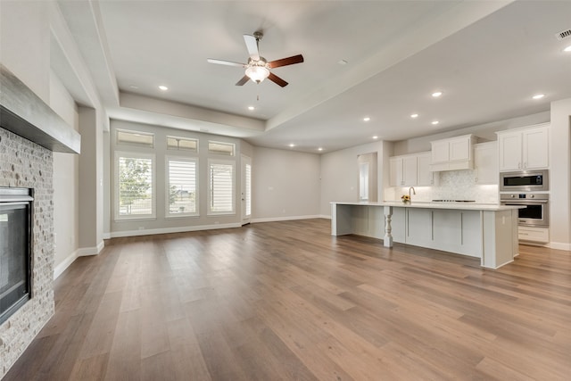 unfurnished living room with ceiling fan, a raised ceiling, sink, a brick fireplace, and light hardwood / wood-style floors