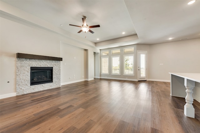 unfurnished living room featuring ceiling fan, dark hardwood / wood-style floors, and a stone fireplace