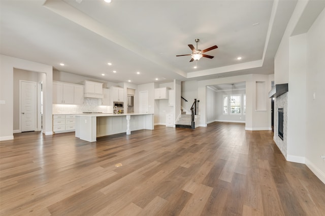 unfurnished living room featuring ceiling fan, a tray ceiling, and light hardwood / wood-style floors