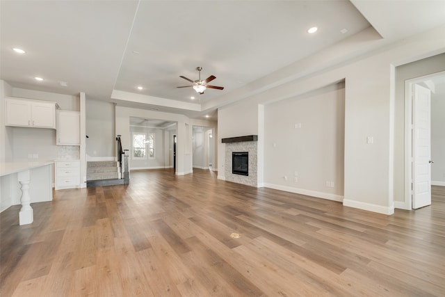 unfurnished living room with light wood-type flooring, a tray ceiling, and ceiling fan