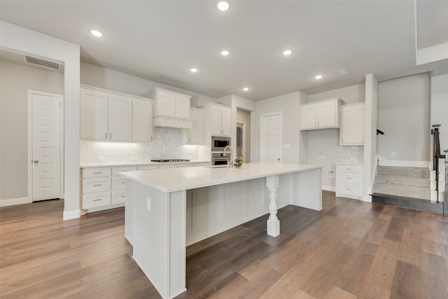 kitchen with white cabinets, hardwood / wood-style floors, stainless steel microwave, and a spacious island