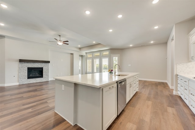 kitchen with sink, stainless steel dishwasher, a kitchen island with sink, white cabinetry, and light wood-type flooring