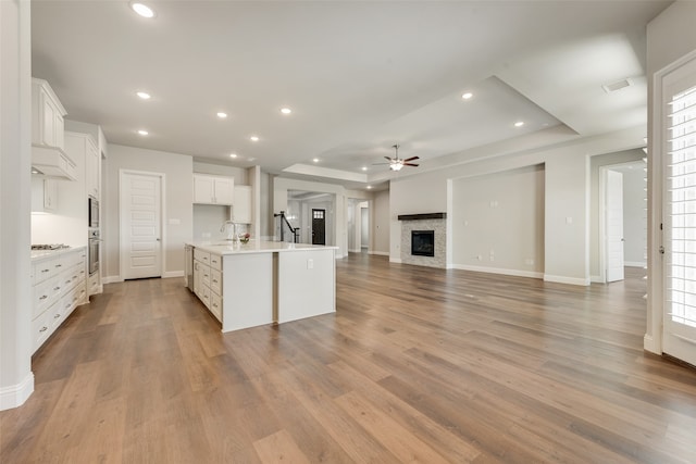 kitchen with a kitchen island with sink, light wood-type flooring, a raised ceiling, and white cabinetry