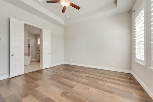 unfurnished bedroom with light hardwood / wood-style floors, multiple windows, a tray ceiling, and ceiling fan