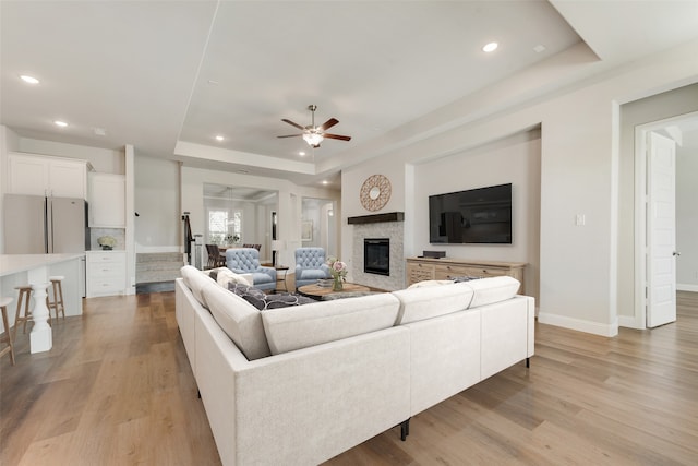 living room featuring ceiling fan, a raised ceiling, and light hardwood / wood-style floors