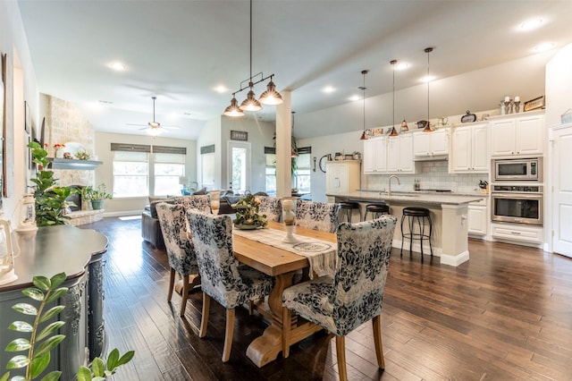 dining room with vaulted ceiling, a fireplace, sink, ceiling fan, and dark wood-type flooring