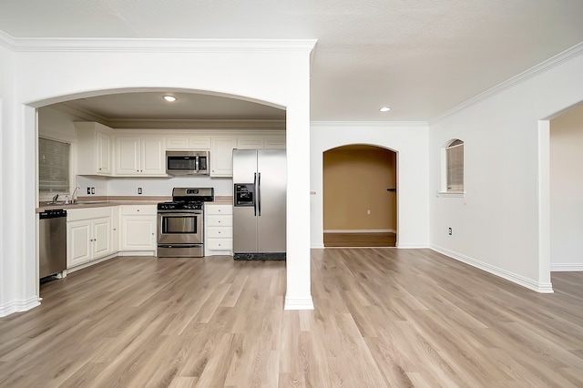 kitchen with light hardwood / wood-style floors, white cabinetry, appliances with stainless steel finishes, ornamental molding, and ornate columns