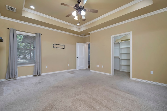 unfurnished bedroom featuring a spacious closet, a tray ceiling, ceiling fan, ornamental molding, and light colored carpet