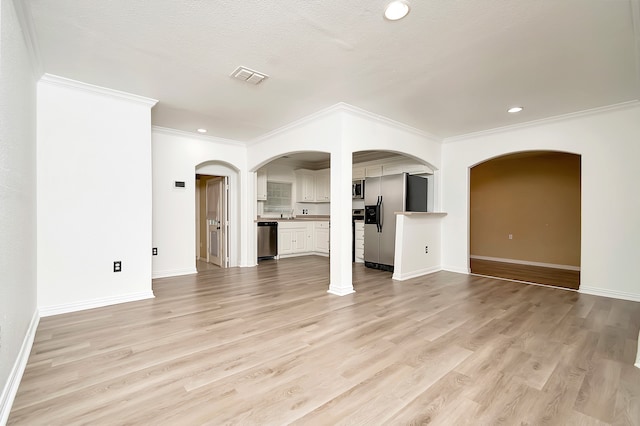 unfurnished living room featuring light wood-type flooring, a textured ceiling, and ornamental molding