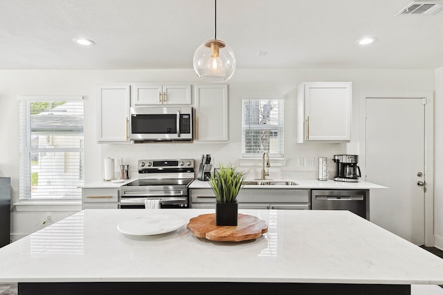 kitchen featuring stainless steel appliances, sink, pendant lighting, white cabinets, and a kitchen island