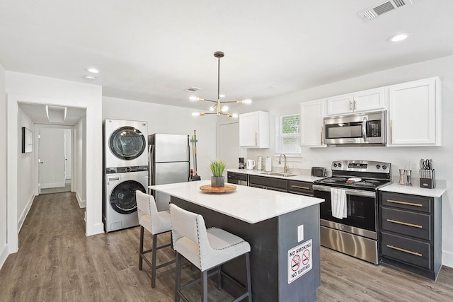 kitchen featuring a center island, sink, stacked washing maching and dryer, white cabinetry, and stainless steel appliances