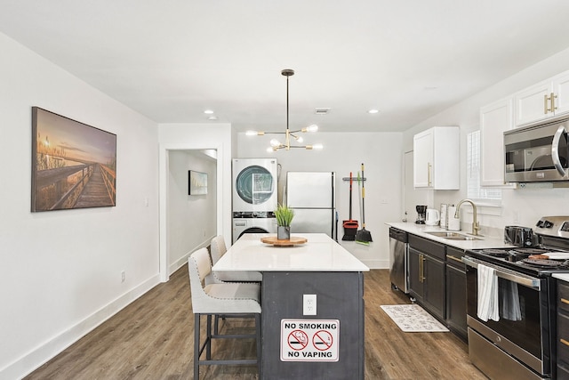 kitchen with appliances with stainless steel finishes, stacked washing maching and dryer, pendant lighting, white cabinets, and a kitchen island