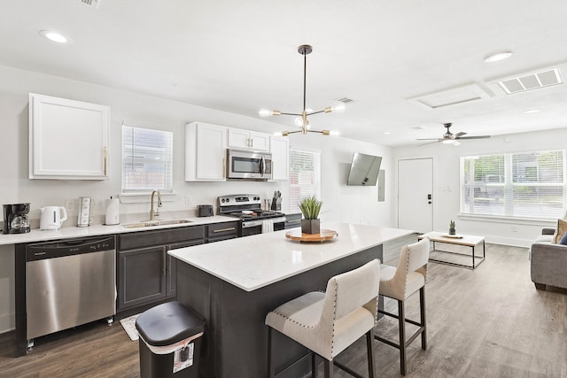 kitchen featuring sink, hanging light fixtures, wood-type flooring, white cabinets, and appliances with stainless steel finishes