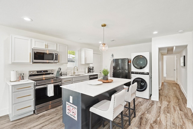 kitchen with stacked washer and clothes dryer, black appliances, white cabinets, sink, and a kitchen island