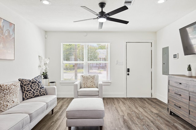 living area featuring recessed lighting, wood finished floors, visible vents, baseboards, and electric panel