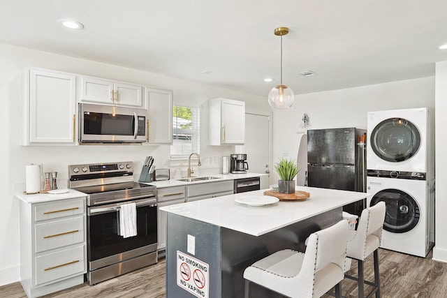 kitchen with sink, black appliances, stacked washer / dryer, white cabinets, and a center island