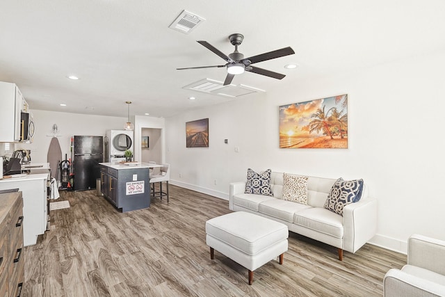 living room with stacked washing maching and dryer, hardwood / wood-style flooring, and ceiling fan