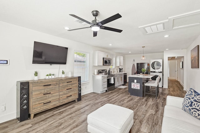 living room with stacked washer / drying machine, ceiling fan, and wood-type flooring