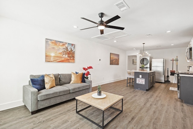 living room featuring light hardwood / wood-style floors, ceiling fan, stacked washer and clothes dryer, and sink