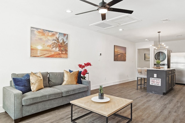 living room with ceiling fan with notable chandelier, stacked washing maching and dryer, and light hardwood / wood-style flooring