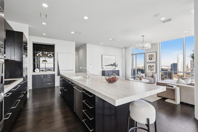 kitchen with sink, hanging light fixtures, dark wood-type flooring, an island with sink, and a chandelier