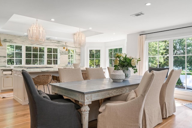 dining room featuring an inviting chandelier, a raised ceiling, and light hardwood / wood-style floors