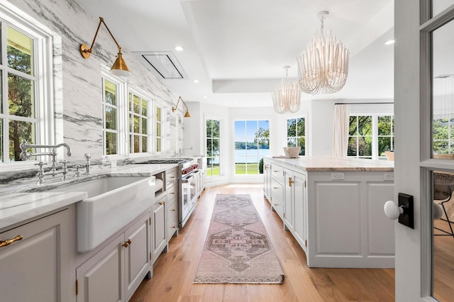 kitchen featuring light stone counters, white cabinets, light wood-type flooring, and pendant lighting