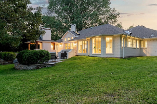 back house at dusk with a patio and a yard