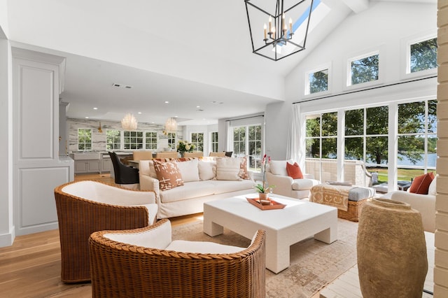 living room featuring an inviting chandelier, light wood-type flooring, high vaulted ceiling, and a healthy amount of sunlight