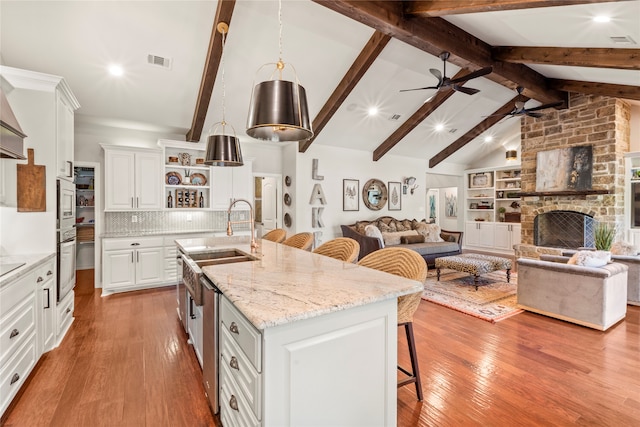 kitchen with a stone fireplace, light wood-type flooring, lofted ceiling with beams, and a kitchen bar