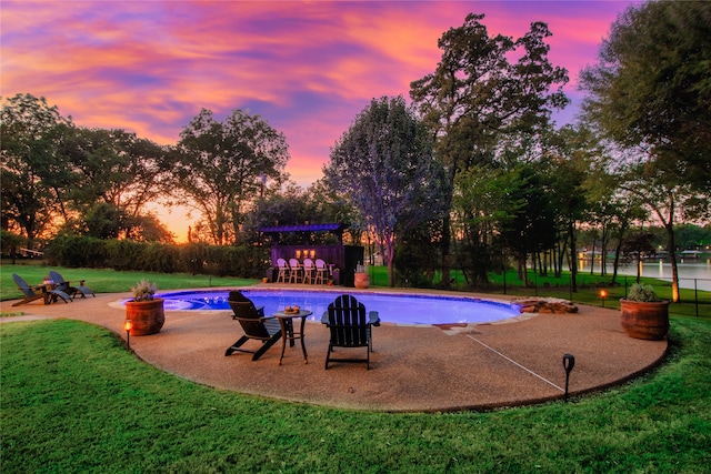 pool at dusk with a lawn and a patio area