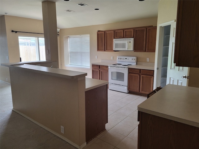 kitchen featuring kitchen peninsula, light tile patterned floors, and white appliances