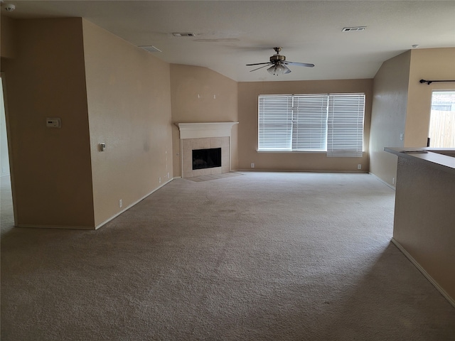 unfurnished living room featuring ceiling fan, light colored carpet, a tiled fireplace, and vaulted ceiling