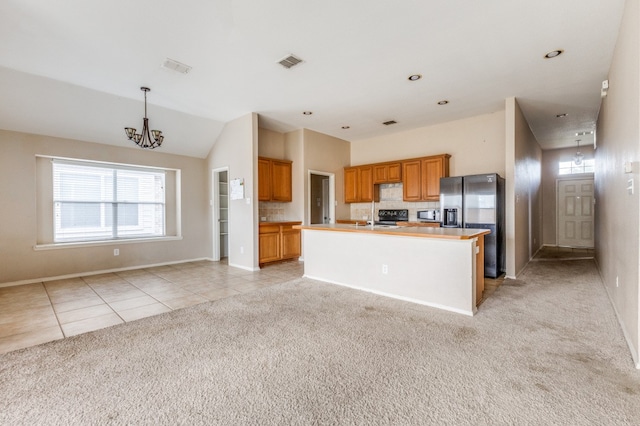 kitchen with light colored carpet, an island with sink, hanging light fixtures, and a healthy amount of sunlight